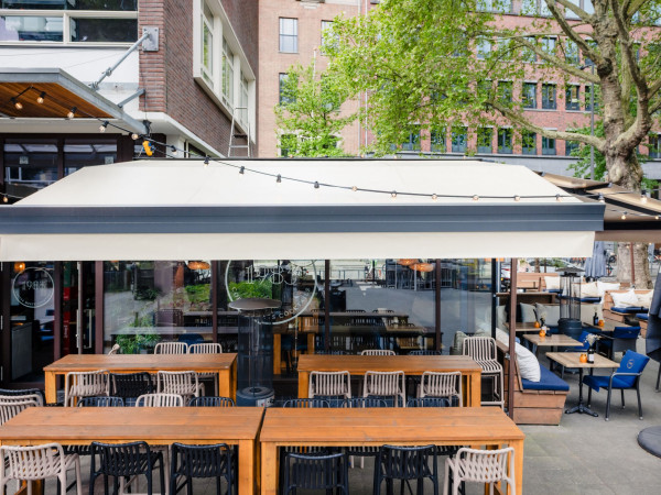 Brede terraszonwering boven het gezellig ingerichte terras van 1983 Bar in Rotterdam.