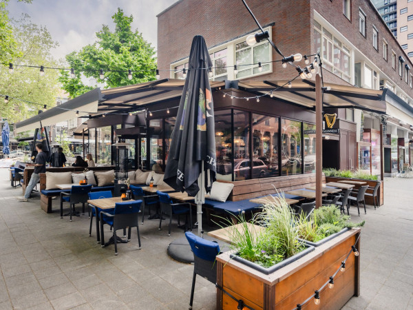 Hoekterras van 1983 Bar met meerdere uitgeschoven zonneschermen rondom de horecagelegenheid.