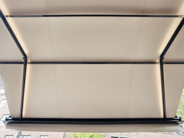 Onderzijde van een uitgeschoven telescoopzonnescherm met zwart armsysteem en licht PVC doek.