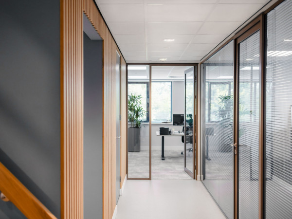 Moderne kantoorgang met glazenwanden en geïntegreerde jaloezieën bij Beko Groothandel.