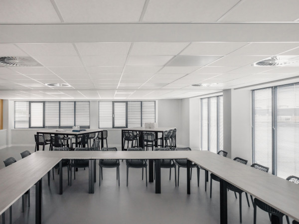 Grote en lichte bedrijfskantine met jaloezieën langs meerdere gevelramen.