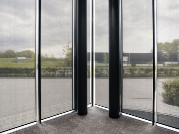 Lichtdoorlatende binnenzonwering voor de hoge hoekramen van het kantoor van DAEL.