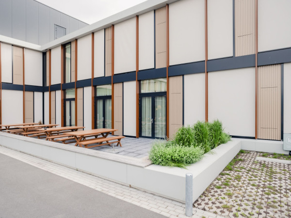 Binnenplaats van Little Dutch met gevelbrede screens, houten geveldelen, picknickbanken en groene beplanting.